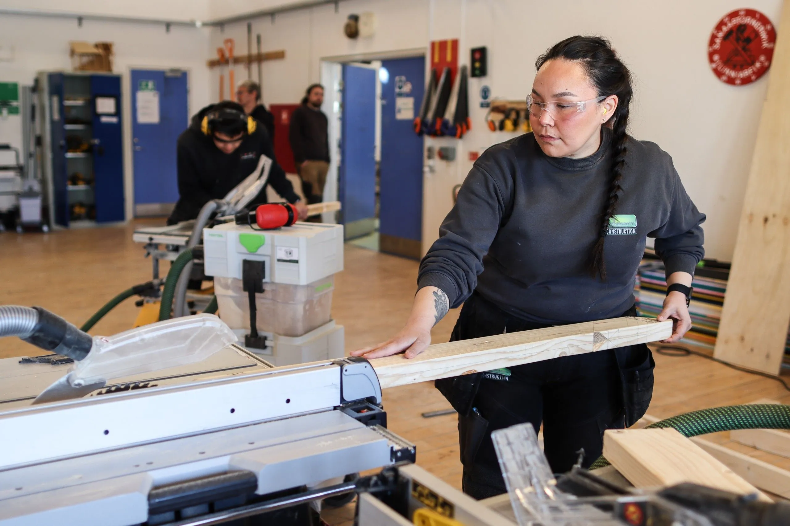 Studerende med sikkerhedsbriller arbejder ved en rundsav i værkstedet.